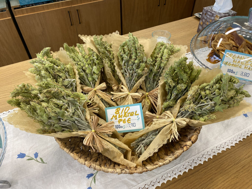 A close-up of Mursal tea leaves, showcasing their unique green color and distinctive shape, displayed on a wooden table with a rustic teapot in the background.